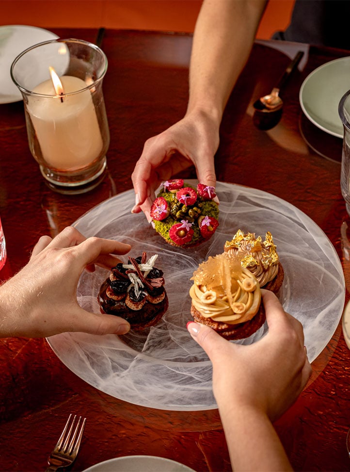 Hands reaching for colourful festive pastries on a shared plate beside a lit candle.