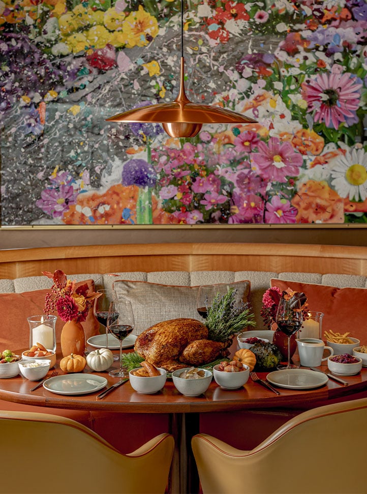 A Thanksgiving-style table set with a roasted turkey, side dishes, wine and autumnal flowers.