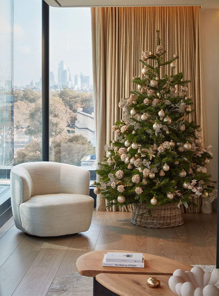 A decorated Christmas tree beside a cream armchair with city views through floor-to-ceiling windows.