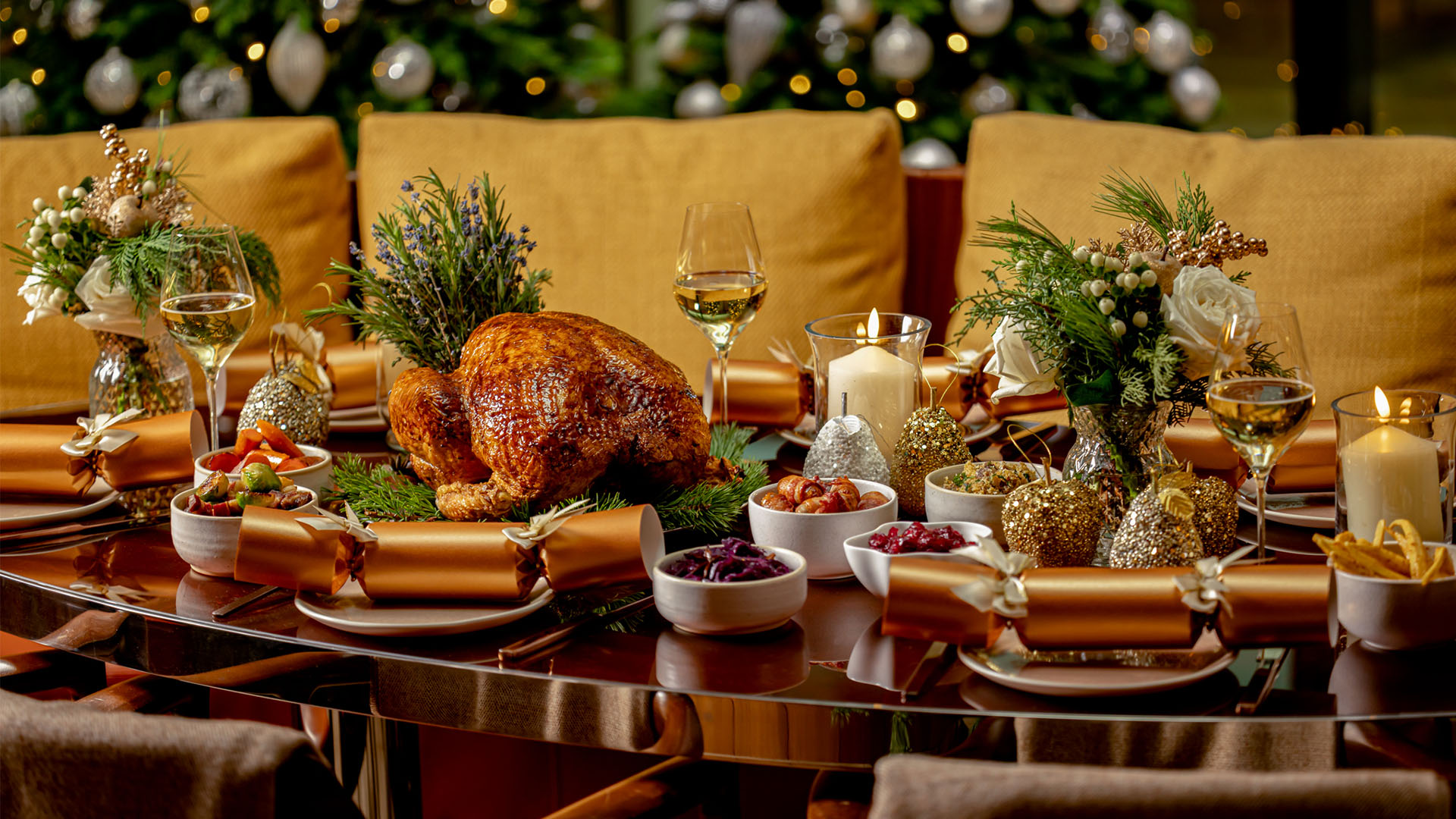 A Christmas table set with a roasted turkey, sides, flowers, candles and gold decorations.