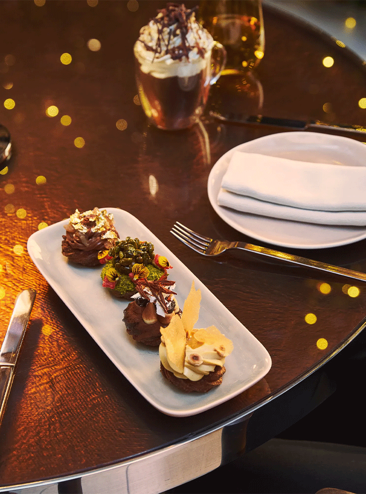 Selection of festive desserts on a rectangular plate beside a place setting, lit by warm candlelight.