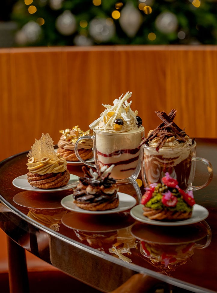 Assorted festive pastries and whipped cream-topped hot drinks on a polished table.