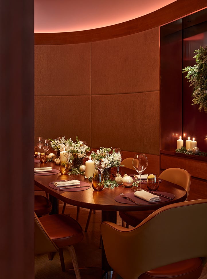 An intimate, warmly lit dining room featuring a beautifully adorned table with festive floral arrangements, candles, and elegant place settings.