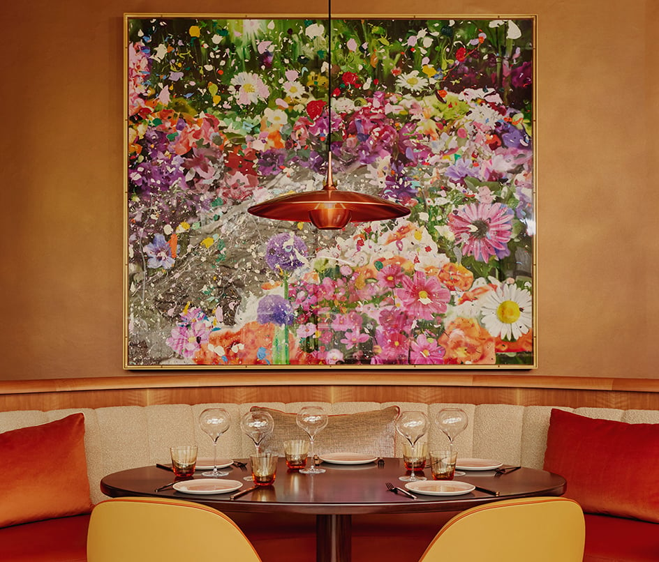 Interior of abc kitchens, a table and chairs sit in front of a large floral painting by Damien Hirst