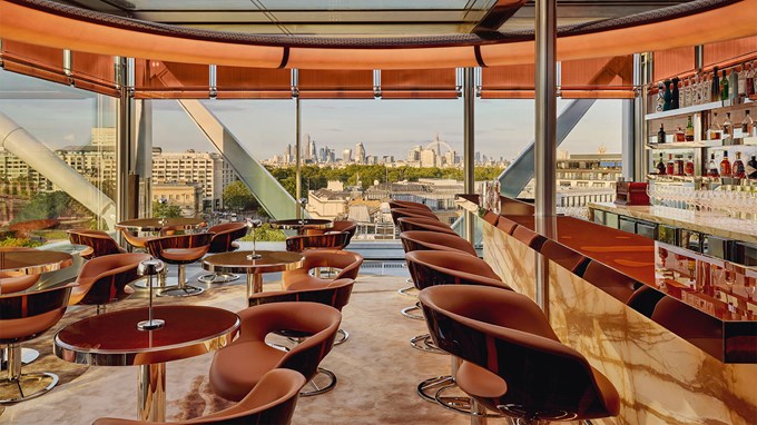 View of Bar 33 with tables and chairs, and the bar with stools tucked underneath. View outside of London''s urban landscape.
