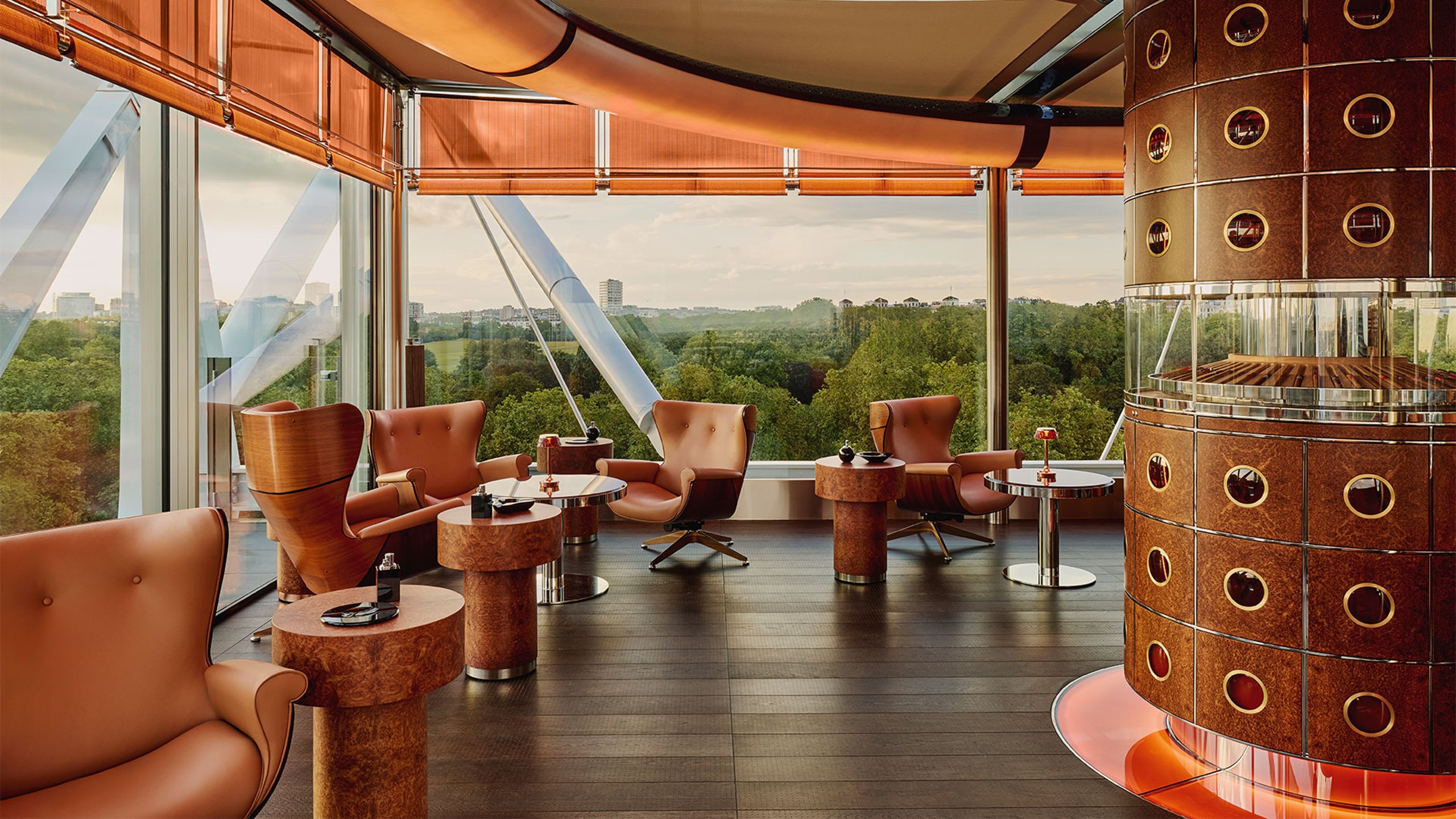 The Emory Cigar Merchant, with displays of cigar in the middle of the room, and arm chairs and small tables dotted around the room. Floor to ceiling windows overlooks Hyde Park.