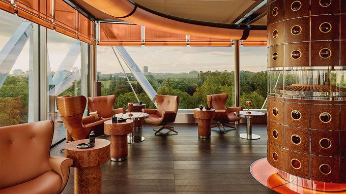 The Emory Cigar Merchant, with displays of cigar in the middle of the room, and arm chairs and small tables dotted around the room. Floor to ceiling windows overlooks Hyde Park.