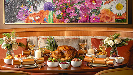 A holiday feast with a roast turkey, wine glasses and crackers on a warmly decorated table.