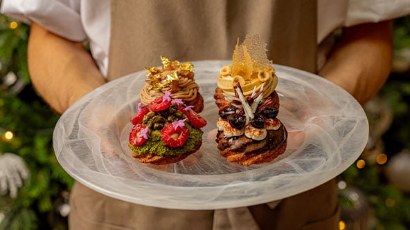 Person holding a frosted plate with three festive pastries decorated with fruit, cream and gold accents