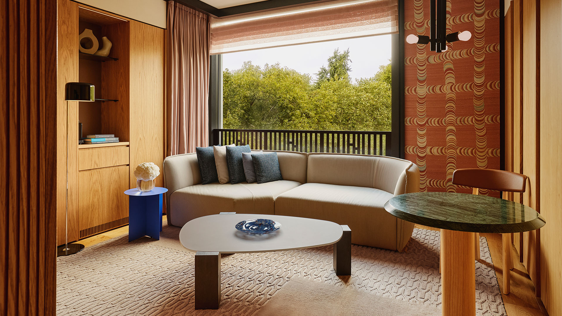 Contemporary suite with sofa adorned with blue cushions, a coffee table, a floor to ceiling window overlooking leafy green trees.