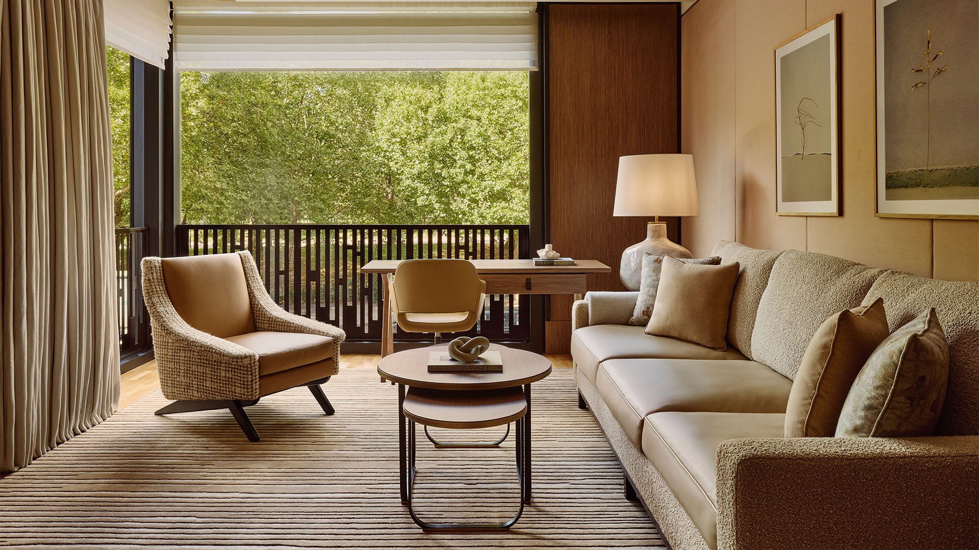 Contemporary suite with a sofa, coffee table, arm chair, desk and desk chair and floor to ceiling windows overlooking leafy green trees.