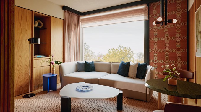 Balcony Park Suite sitting area. A large window sits in the background and a couch sits infront. A round wooden table with a plate sits in the foreground.  A round marble and wooden table with a plant and two chairs sit on the right.