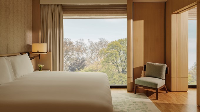 Bedroom of the Corner Park Suite with white  bedding on the large bed facing out towards floor to ceiling windows revealing the trees and park outside