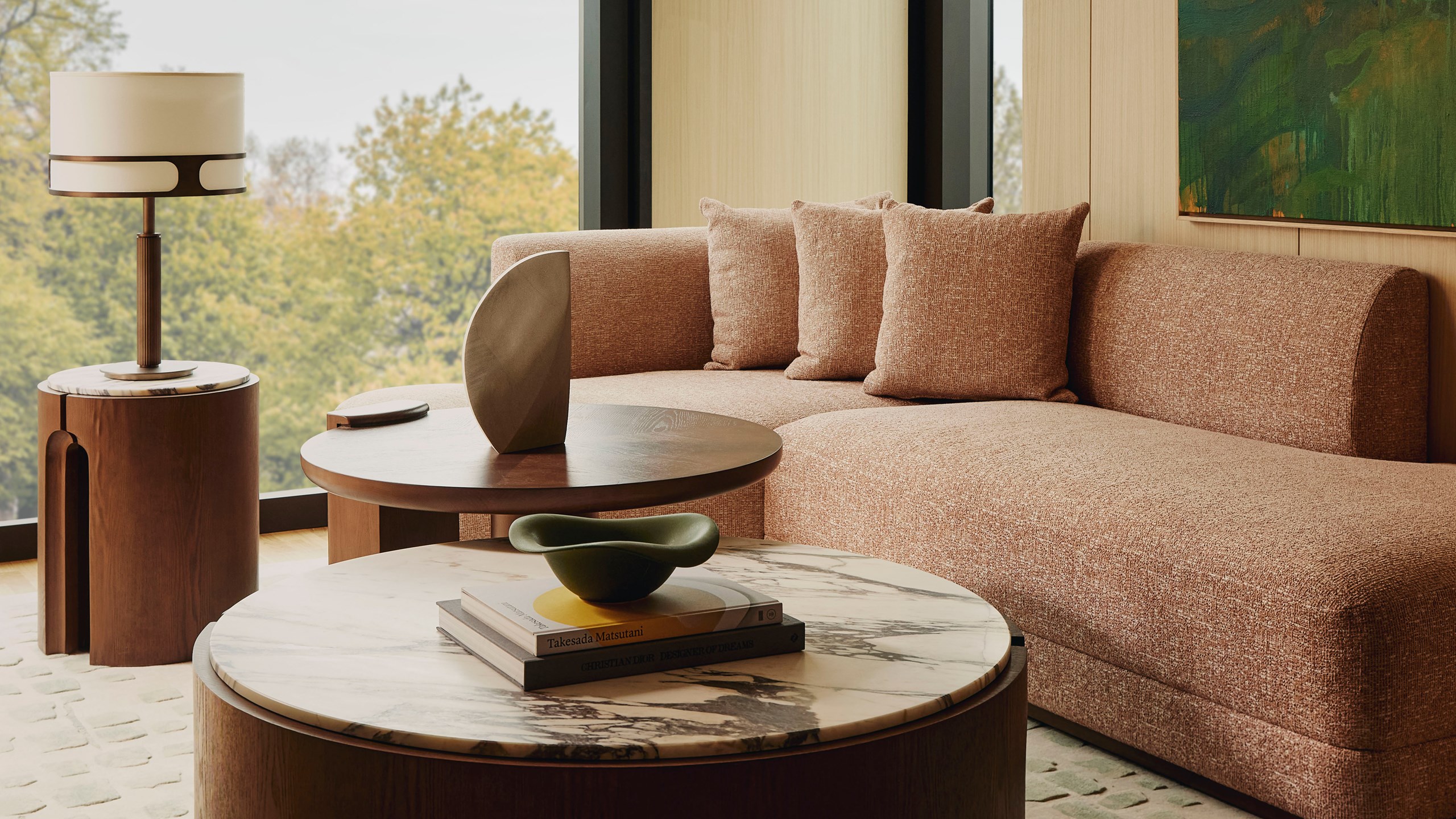 The Emory Corner Park Suite sitting area - A window sits to the left. A couch with three cushions sits in front of it. A round wooden and marble table with a lamp sits to the left.