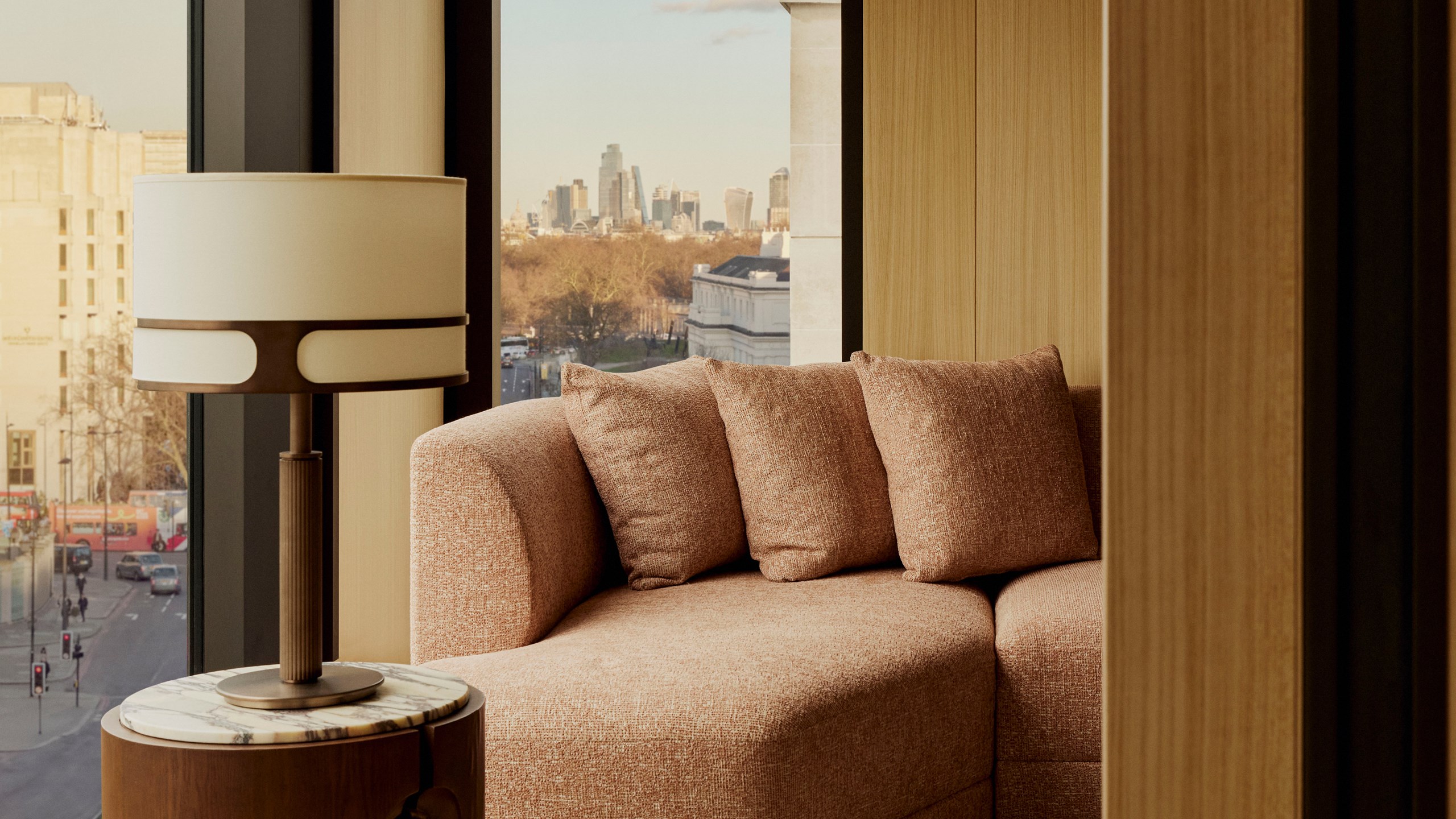 The Emory Corner Park Suite sitting area - A window sits to the left. A couch with three cushions sits in front of it. A lamp sits to the left.