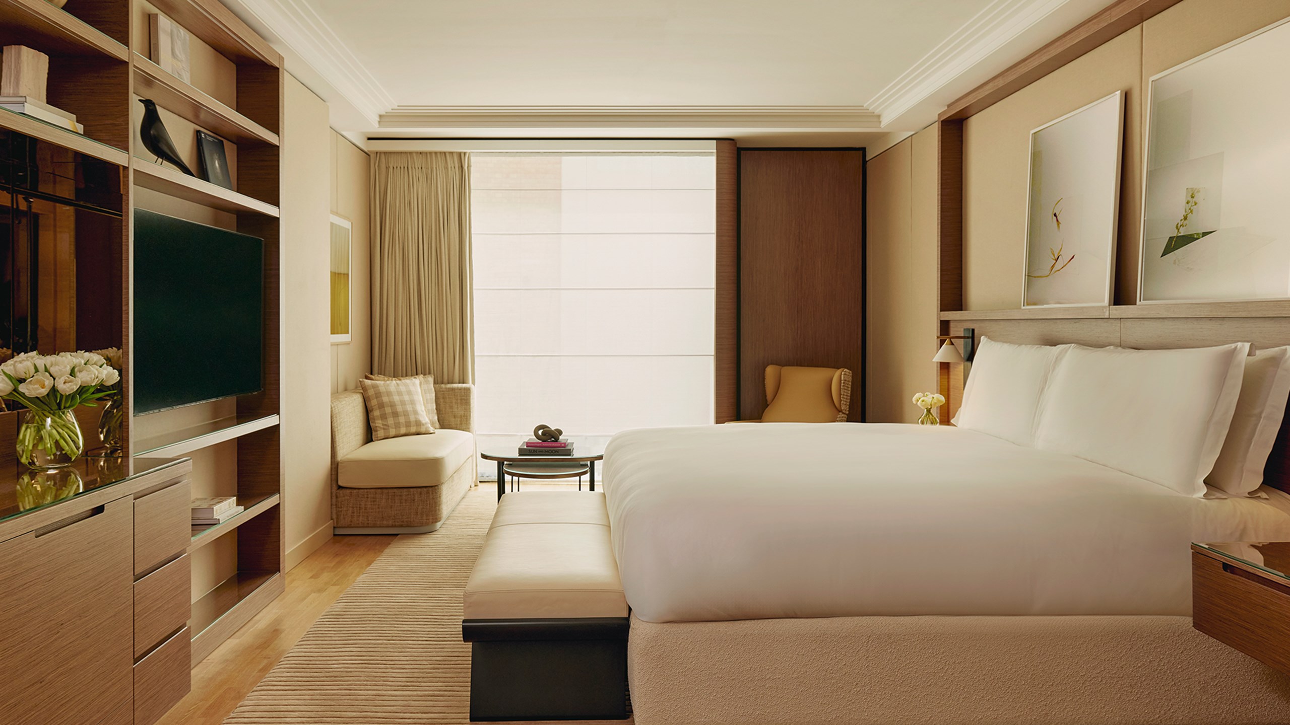 Bedroom of suite, with beige and cream decor, a large bed in the middle looking towards a television on the wall