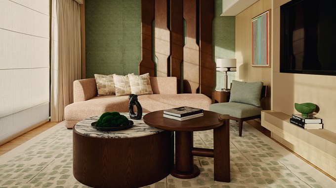 Courtyard Junior Suite living area. A window is to the left and a circular wood and marble table with a plant and books is in the foreground. A sofa and chair sit behind it.