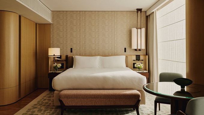 Courtyard Junior Suite bedroom. A window is to the right and a double bed is in the foreground. A bench sits at the end of the bed. Two bedside tables sit on either side of the bed with flowers sitting on top.