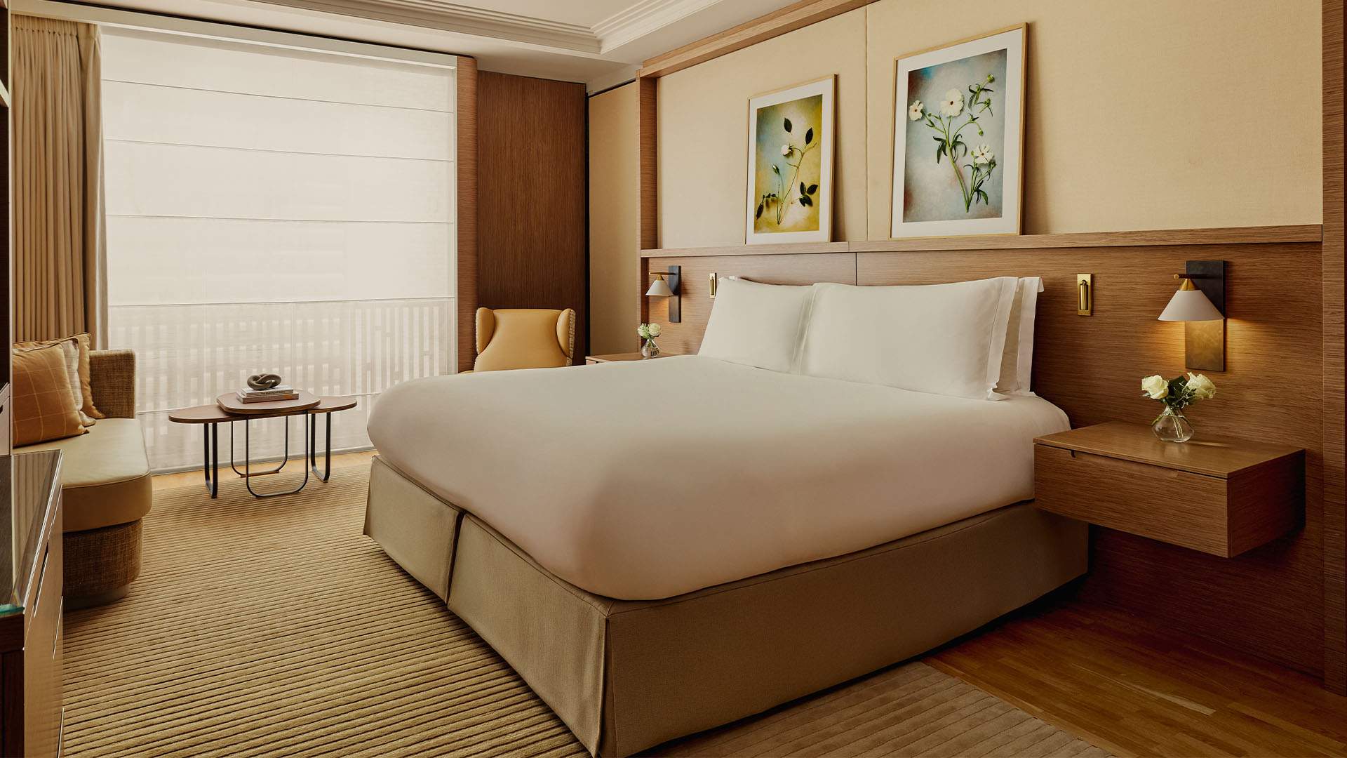 Soft, neutral bedroom with a large bed, floral artwork, built-in seating, and filtered daylight through sheer blinds