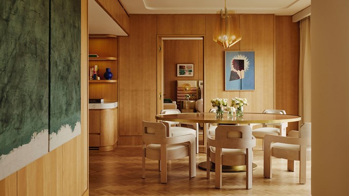 Wooden dining table and chairs in the middle of the dining room, covered in wooden panels with modern art on the walls.