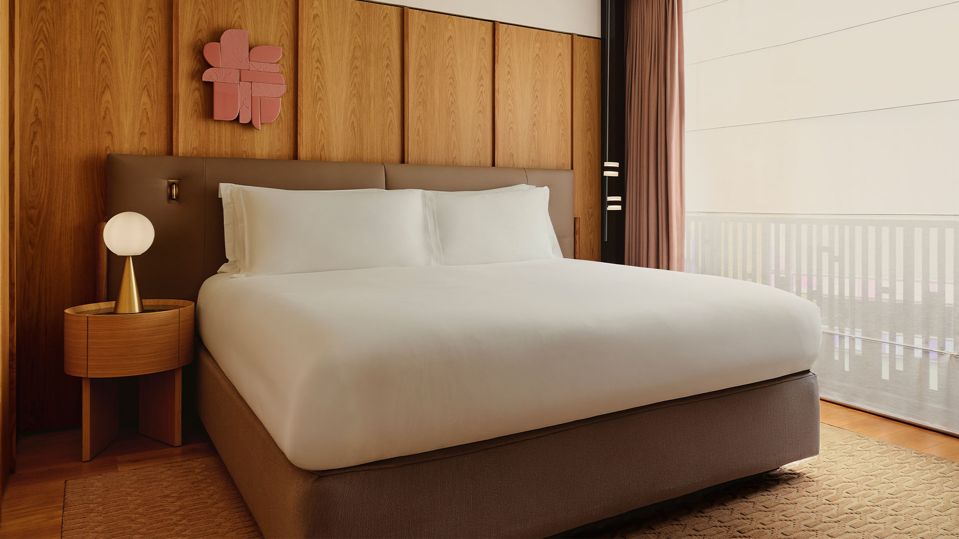 Warm bedroom with a large bed, wood panelled walls, round bedside table, and soft filtered light.