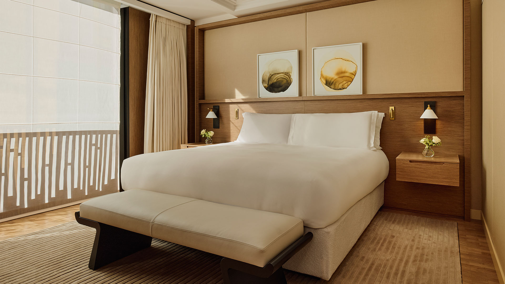 Calm bedroom with large bed, bench, framed abstract art, and soft daylight through sheer blinds