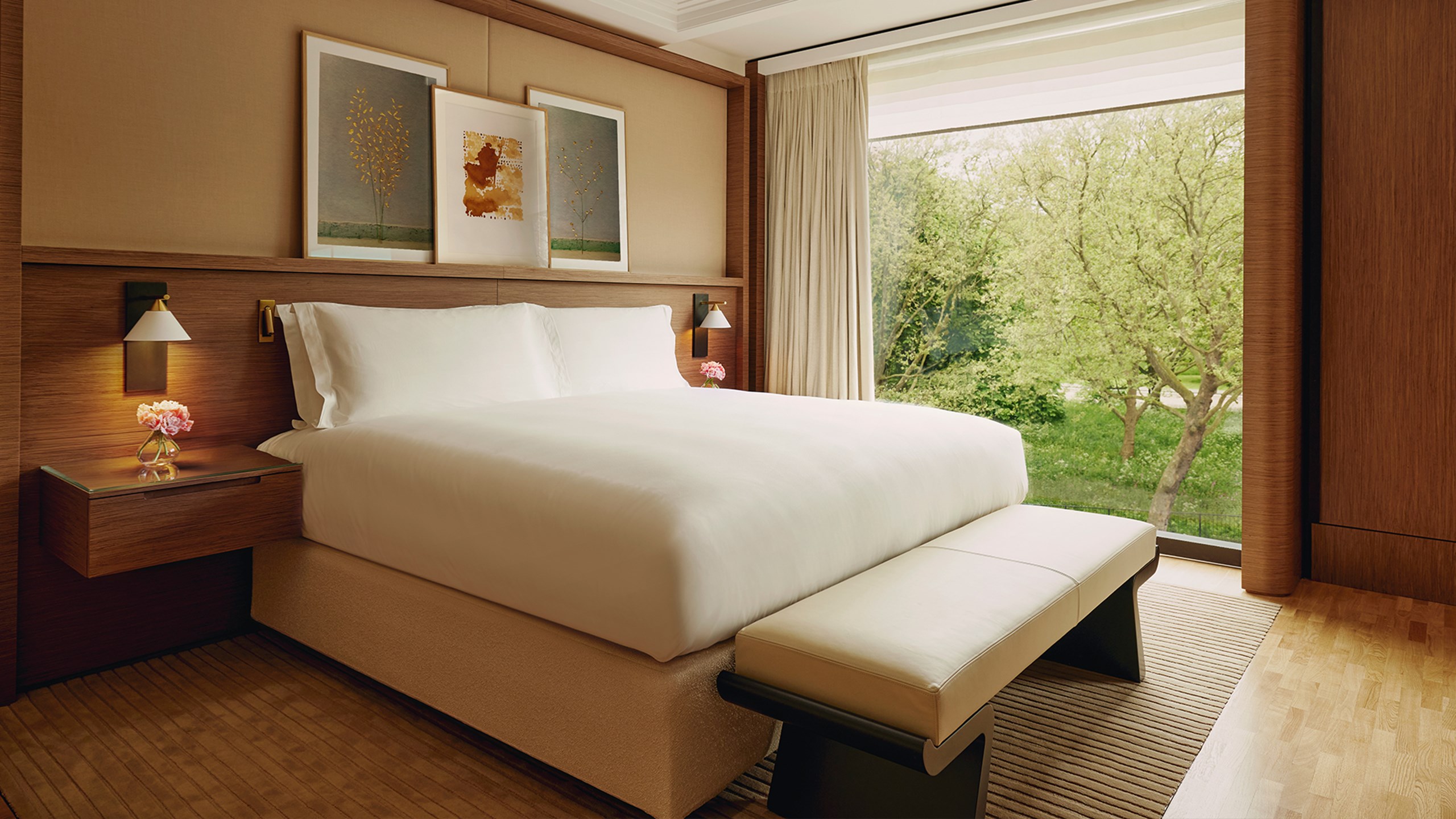 King size bed placed in front of floor to ceiling window looking out towards a park view