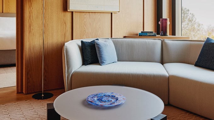 The edge of a grey sofa with a variety of blue cushions placed on top, with wooden panelling behind
