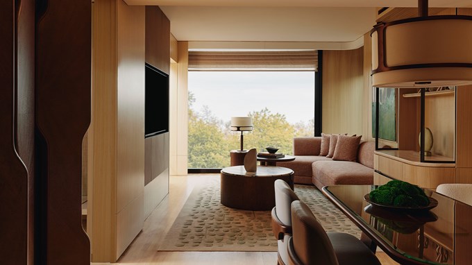 A refined living space with modern furnishings, featuring a curved sectional sofa, rich wooden accents, and floor-to-ceiling windows offering serene views of lush greenery.