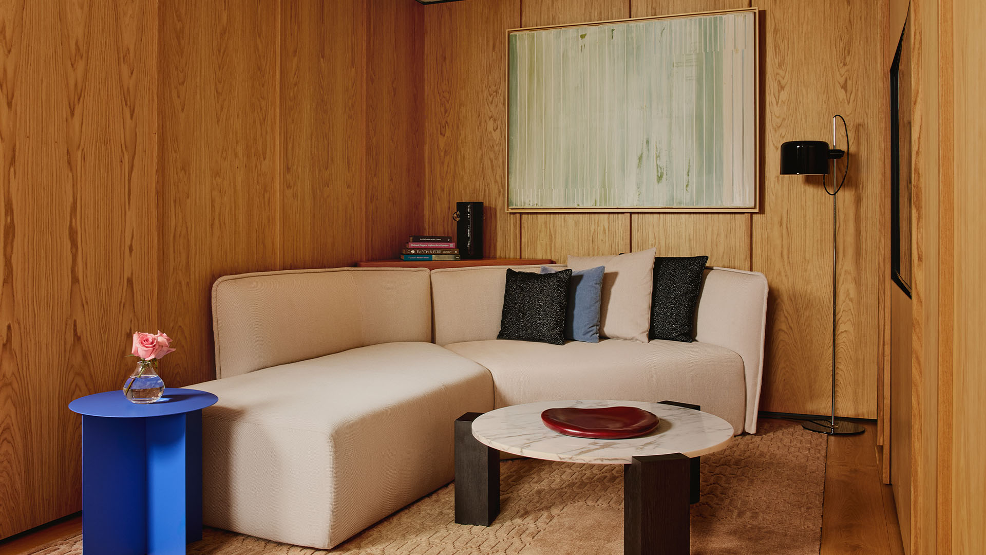 Cosy wood-panelled lounge with cream corner sofa, blue side table, and abstract artwork above.