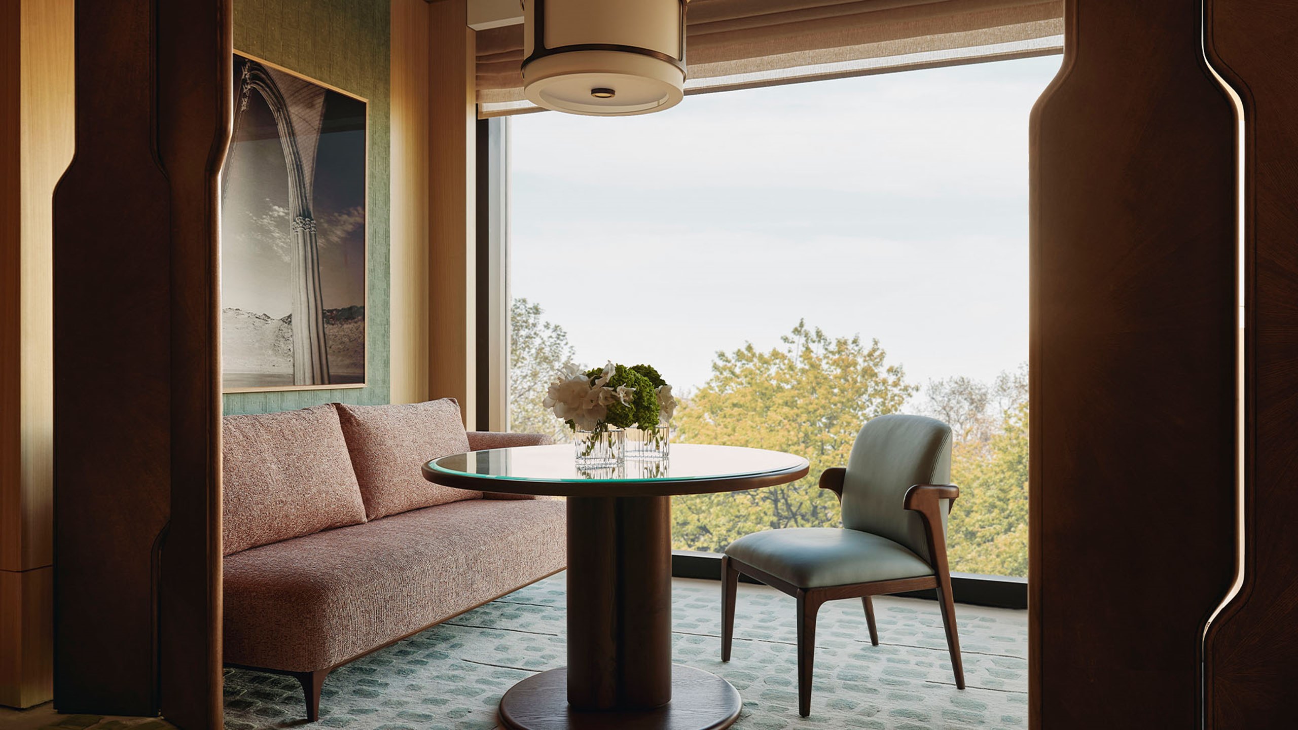 Park Junior Suite sitting area. A window sits in the background and a glass and a couch sits beside it. A circular wooden and glass table sits in front of the couch and a chair sits beside it.
