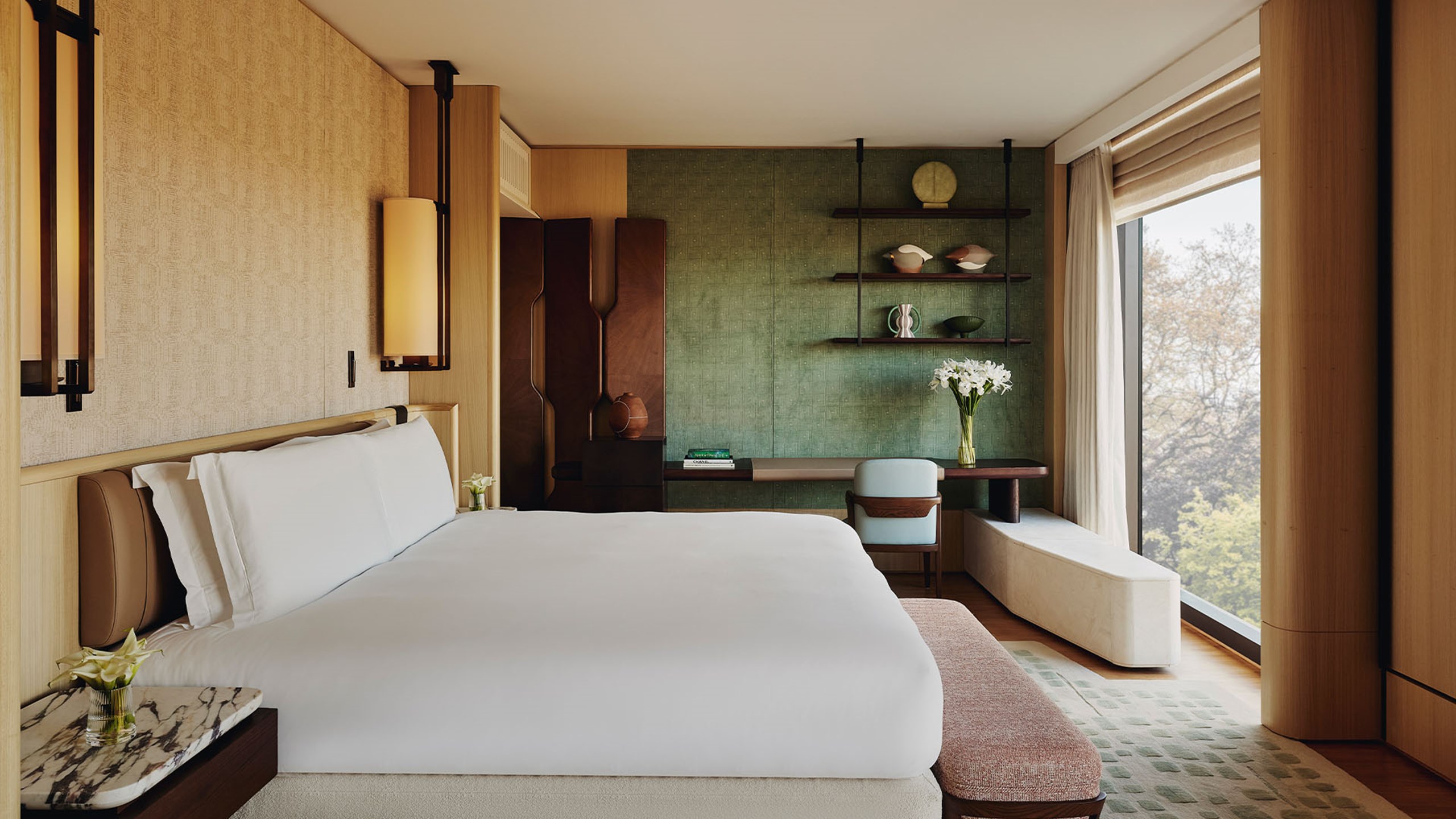 Bedroom of The Emory Park Suite with high white bed facing glass windows revealing the trees and park outside,