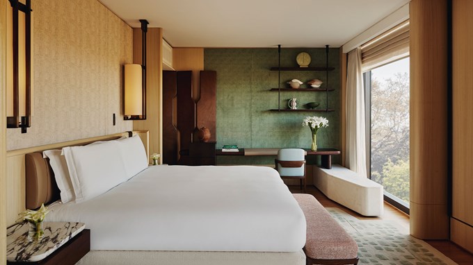 Bedroom of The Emory Park Suite with high white bed facing glass windows revealing the trees and park outside,