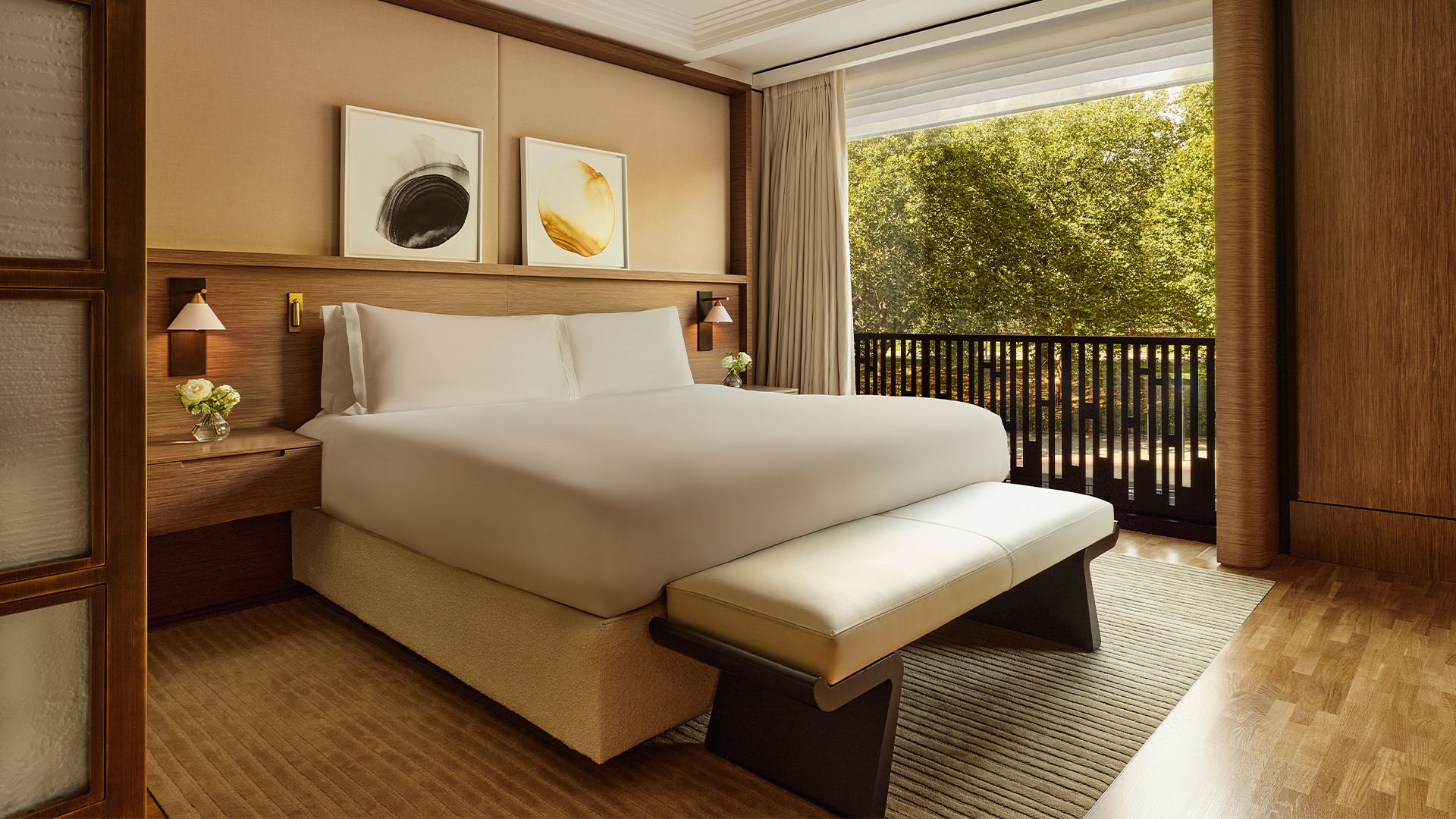 Serene bedroom with a large bed, warm wood accents and balcony overlooking leafy park views